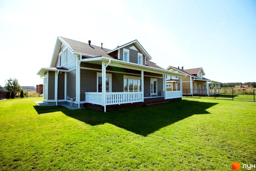 Двоповерховий будинок з коричневою покрівлею та білими віконними рамами. Перед будинком доглянутий газон, збоку видно ще один будинок.