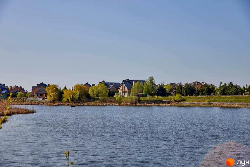 Котеджне містечко Вишневе містечко. Фото новобудов біля озера з деревами та зеленим газоном. Забудова складається з цегляних будинків з темними дахами.