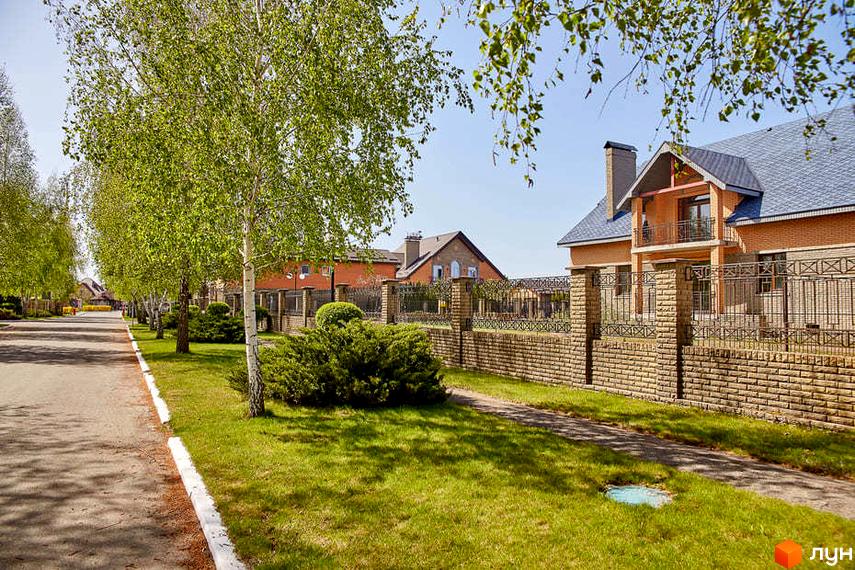 Котеджне містечко КМ Вишневе містечко: цегляні будинки з балконами та сірими дахами, огороджені кам'яним парканом. Прибудинкова територія з зеленими газонами, кущами та деревами.