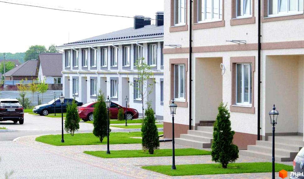 Фасади котеджів Котеджного містечка Паларіс світлого кольору з коричневим оздобленням. Перед будинками доглянуті газони та бруківка.