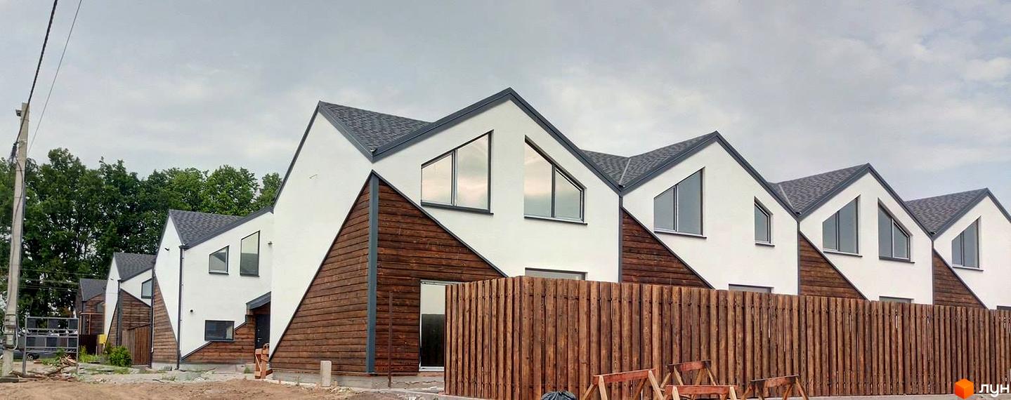 Зовнішній вигляд таунхаусів «Кримський квартал» з білими стінами, дерев'яним оздобленням та сірими дахами. Навколо дерев'яний паркан.
