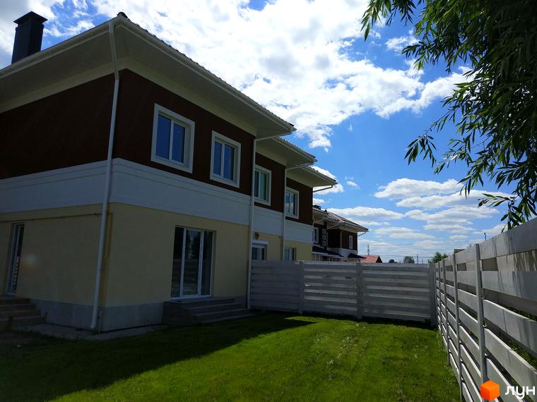 Таунхауси „Плюс“ – двоповерхові будинки з коричневою та світлою обробкою фасаду. Навколо будівель зелений газон та білий дерев'яний паркан.