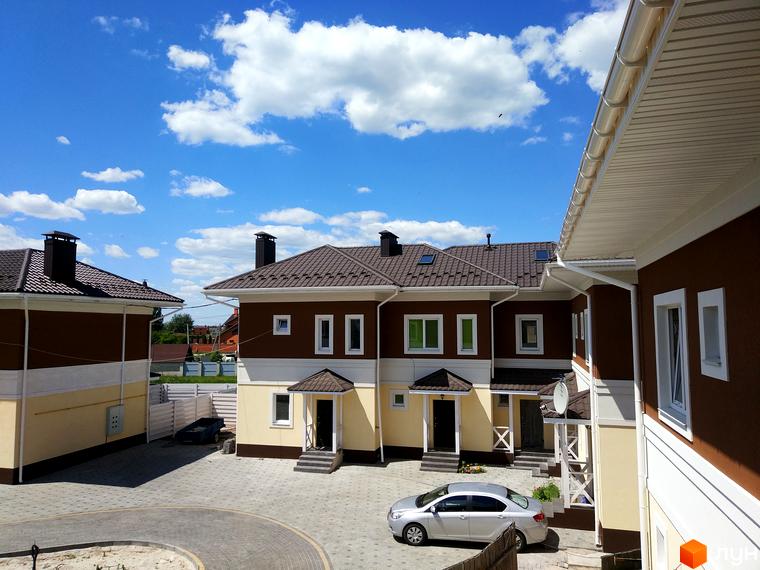 Таунхауси „Плюс“ – новобудова з коричнево-жовтими фасадами та коричневим дахом. Прибудинкова територія з бруківкою та автомобілем.