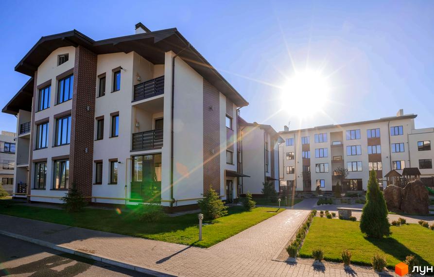 Новобудова Клеменова Дача з багатоповерховими будинками світлого кольору та темними дахами. На території комплексу розташовані зелені газони, доріжки та дитячий майданчик.