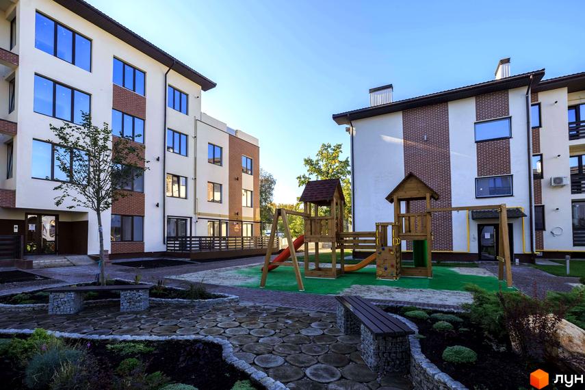 Житловий комплекс Клеменова Дача: фасади будинків зі світлою штукатуркою та цегляними вставками, двір з дитячим майданчиком та ландшафтним дизайном.