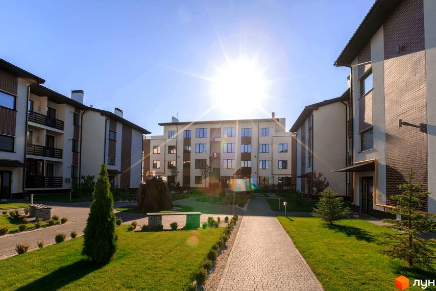 Житловий комплекс Клеменова Дача: багатоповерхові будинки світлих відтінків з цегляними вставками. Доглянута прибудинкова територія з газонами, доріжками та зеленими насадженнями.