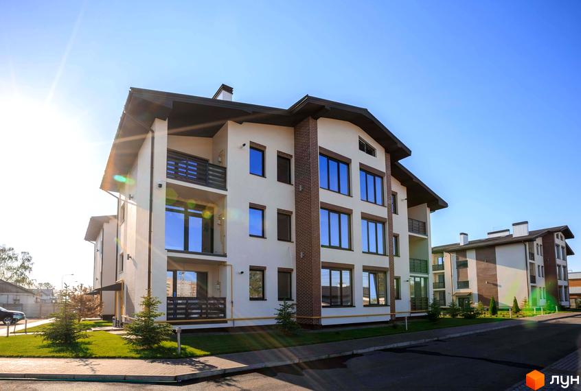 Житловий комплекс Клеменова Дача з будинками світлого кольору, темними дахами та вікнами, балконами. Навколо зелені газони та молоді дерева.