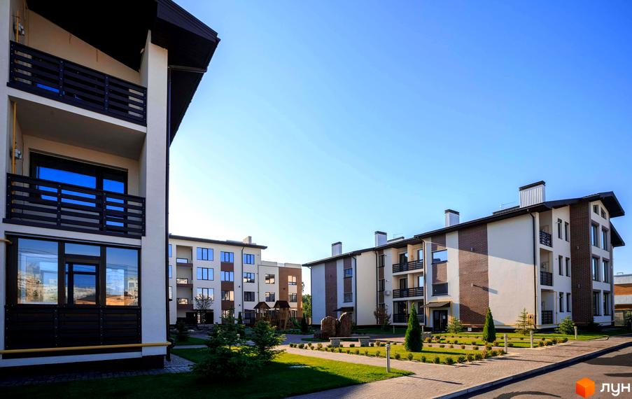 Житловий комплекс Клеменова Дача: багатоповерхові будинки світлого кольору з цегляними вставками та темними балконами. Прибудинкова територія з газонами, доріжками, деревами.