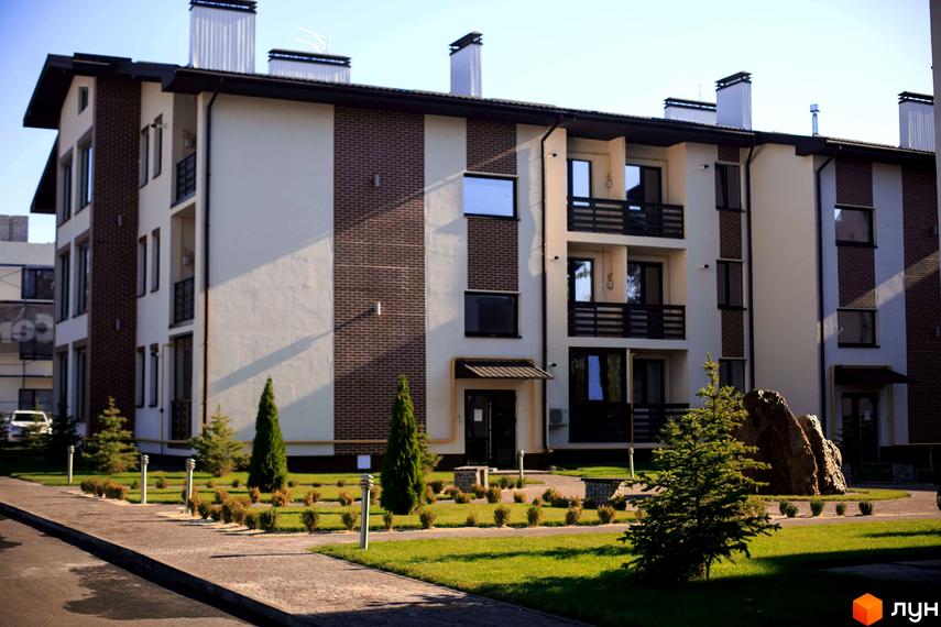 Житловий комплекс Клеменова Дача: багатоповерховий будинок з бежевим фасадом, цегляними вставками та балконами. Прибудинкова територія з газоном, деревами, кущами та каменем.