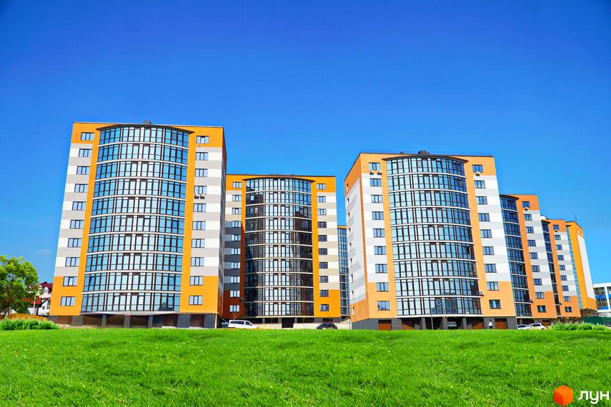 Зображення фасаду та прибудинкової території Житлового комплексу Містечко Соборне. Багатоповерхові будинки з великими вікнами та зелений газон.