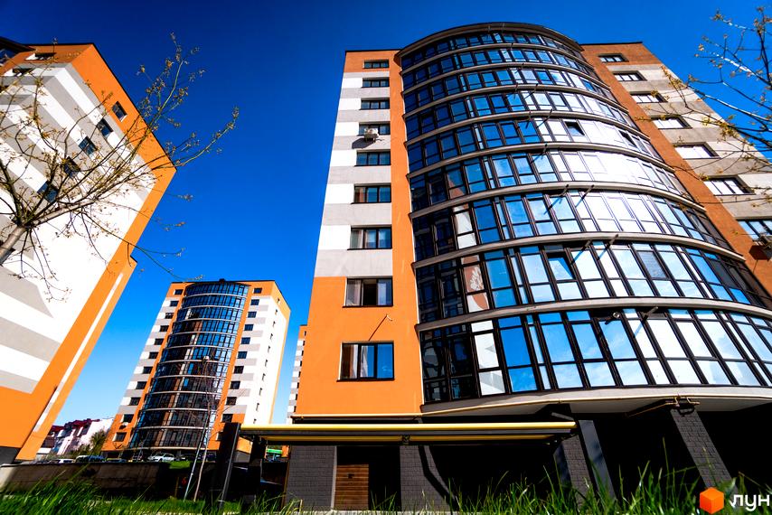 Зображення фасаду та скляних балконів Новобудови Містечко Соборне. Вид на житловий комплекс з газоном.