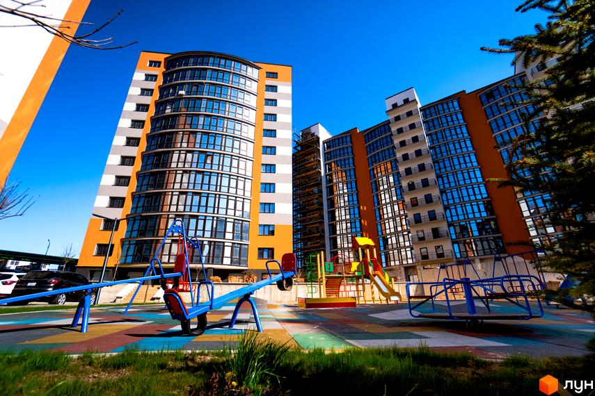 Зображення житлового комплексу Містечко Соборне з яскравим фасадом та дитячим майданчиком. Вигляд новобудови з прибудинковою територією.