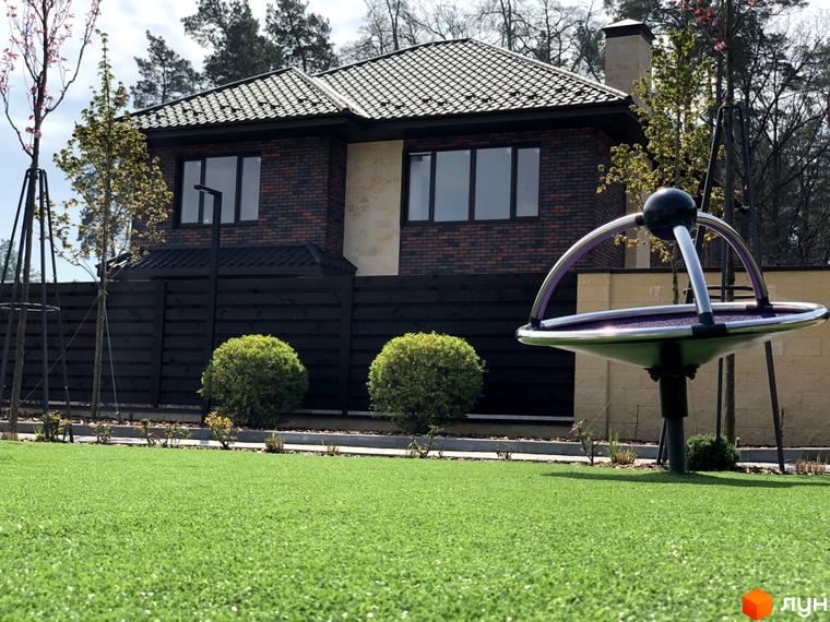 Котеджне містечко Zahrava Village: двоповерховий будинок з цегляним фасадом, великими вікнами та зеленою прибудинковою територією з дитячим майданчиком.