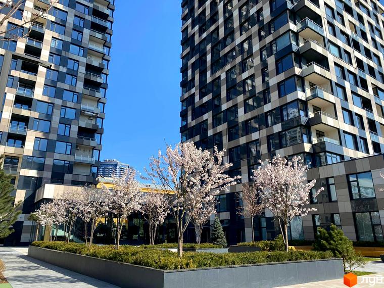 Житловий комплекс Tetris Hall з фасадами з темних та світлих панелей. На прибудинковій території висаджені квітучі дерева та зелені кущі.