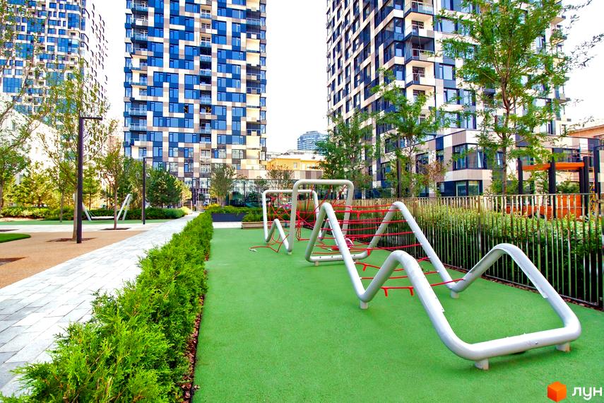 Житловий комплекс Tetris Hall: сучасний дитячий майданчик з гірками та канатними конструкціями на тлі висотних будинків з панорамними вікнами. Прибудинкова територія з доглянутими зеленими насадженнями та доріжками.