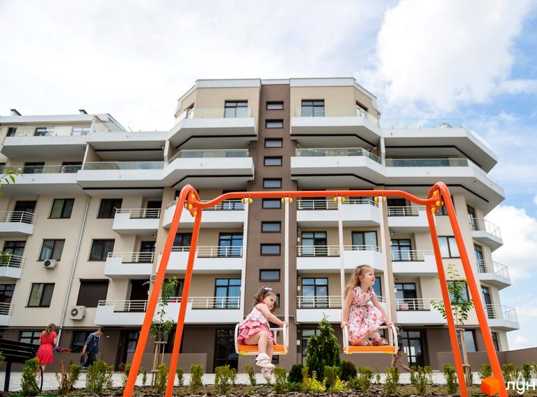 Новобудова GREEN LAND з численними балконами та вікнами. На прибудинковій території розташований дитячий майданчик з гойдалками.