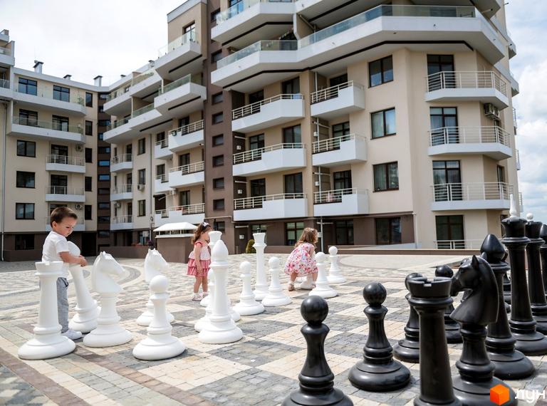 Житловий комплекс GREEN LAND: багатоповерхові будинки з балконами та гігантськими шахами на прибудинковій території. Діти грають на майданчику.