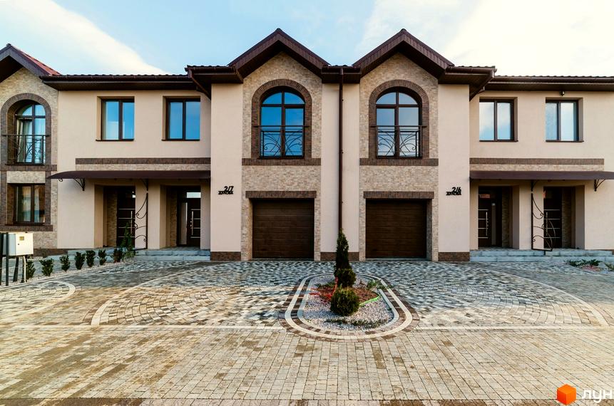 Таунхаус „ДУЛОВА“ з двома поверхами, арочними вікнами та цегляним оздобленням. Прибудинкова територія вимощена бруківкою з декоративною клумбою.