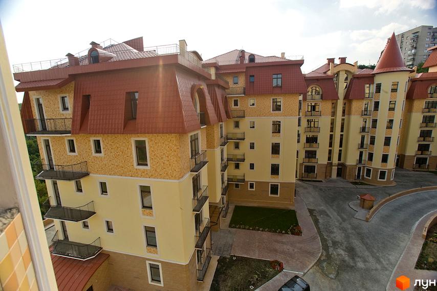 Зображення житлового комплексу Альпійське містечко з будинками світло-жовтого кольору, коричневими дахами та балконами. На території є вимощені доріжки та зелені газони.