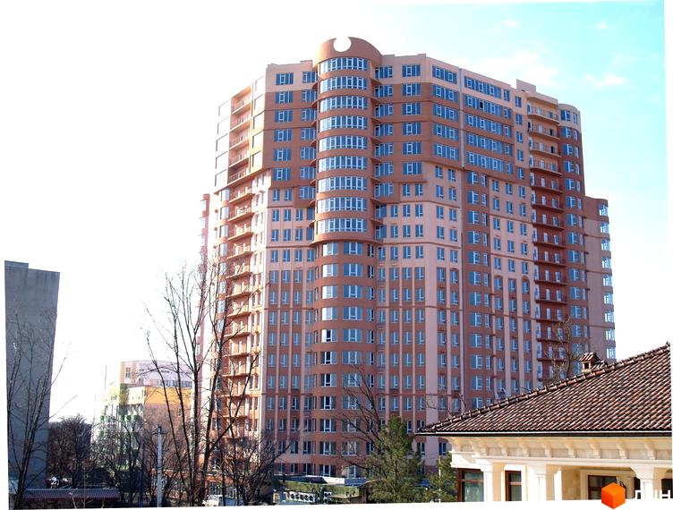 Багатоповерховий житловий комплекс Фонтан світло-коричневого кольору з вигнутим фасадом та балконами. Навколо видно голі дерева та дах сусідньої будівлі.