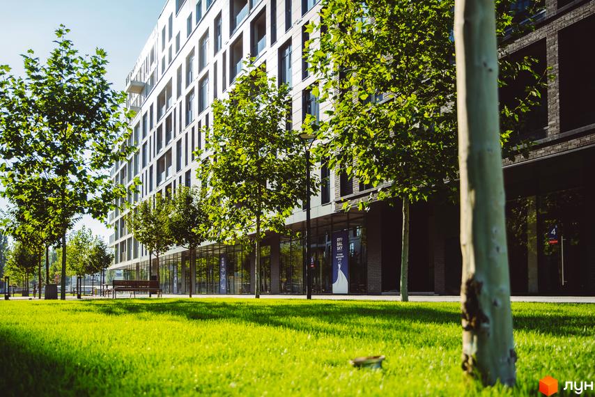 Багатоповерховий будинок Житлового району Rybalsky зі світлим фасадом та великими вікнами. Перед ним зелений газон та молоді дерева.