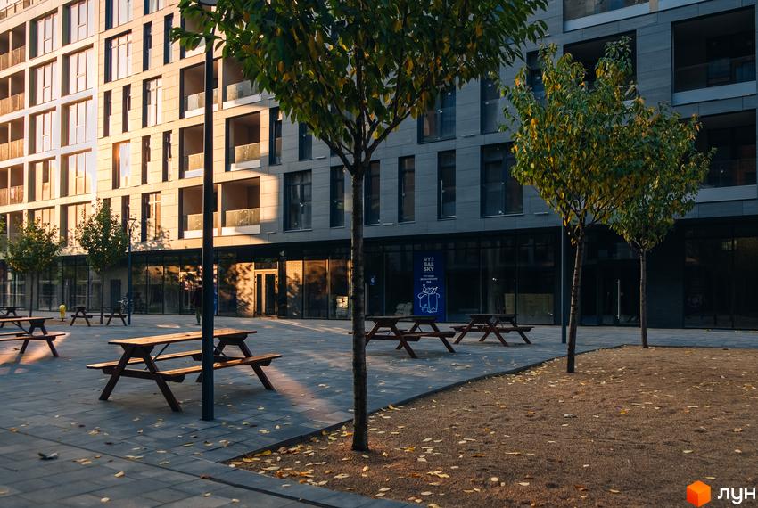 Житловий район Rybalsky: фасади будівель з великою кількістю вікон та балконів, упорядкована прибудинкова територія з лавками, деревами та бруківкою.