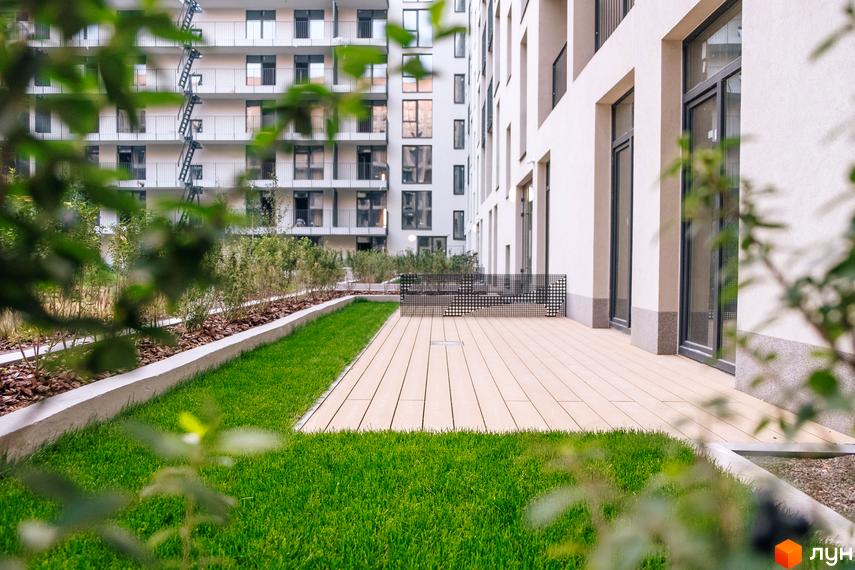 Фасад будинку Житлового району Rybalsky з великими вікнами та балконами. Прибудинкова територія з газоном, терасою та зеленими насадженнями.