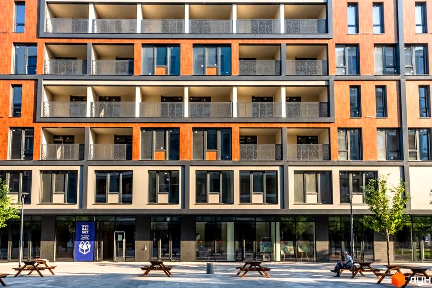 Житловий район Rybalsky - сучасна новобудова з дерев'яними фасадами та балконами. Перед будинком розташовані лавки та столики для відпочинку.