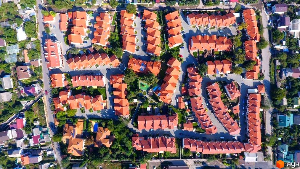 Вид зверху на Котеджне містечко Біла Квітка з типовими будинками з червоними дахами. Навколо будинків зелені насадження та дороги.