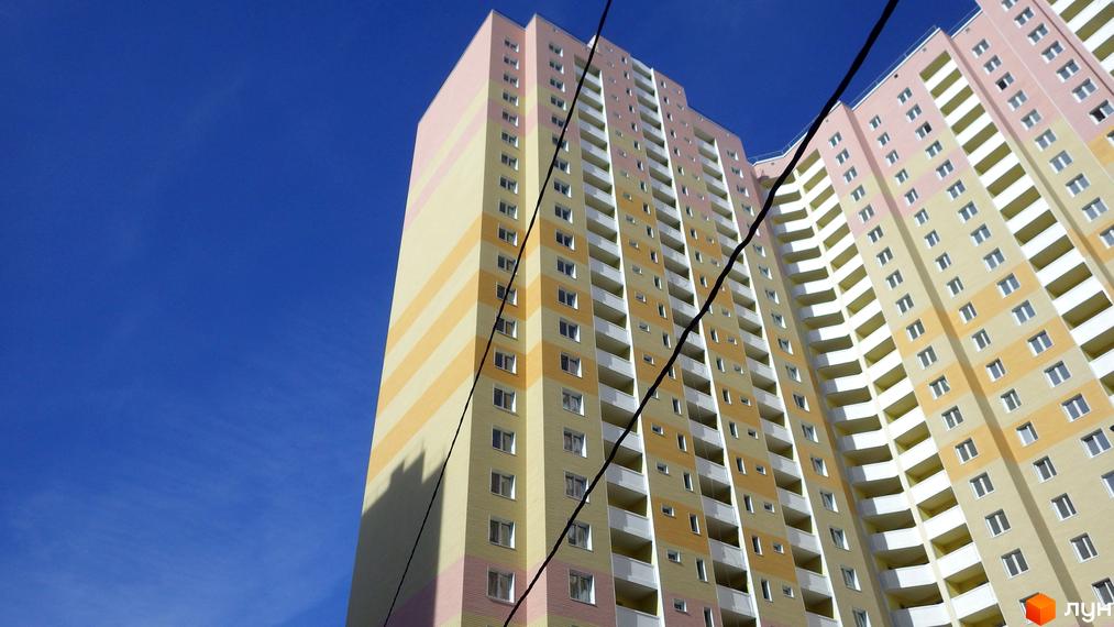 Вид на висотний будинок житлового комплексу Милославичі з кольоровим фасадом. На фоні ясне небо та електропроводи.