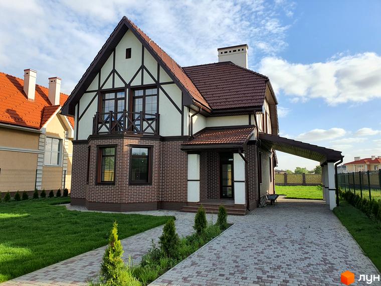 Зображення будинку в Котеджному містечку Осокор. Двоповерховий будинок з червоної цегли з коричневим дахом та зеленою галявиною.