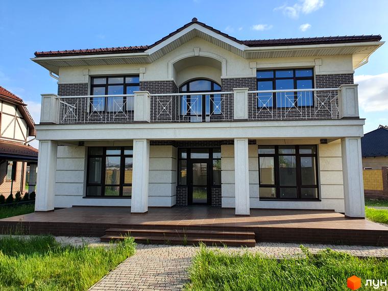 Двоповерховий будинок з великими вікнами та балконом. Перед будинком доглянута прибудинкова територія з газоном та бруківкою.