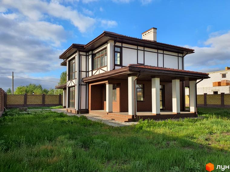 Двоповерховий будинок в Котеджному містечку Осокорки з коричневим дахом та колонами. Зелений газон перед будинком.