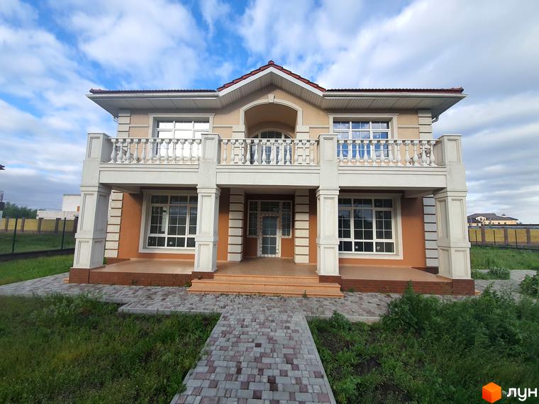 Двоповерховий будинок з балконом та колонами. Перед будинком викладена доріжка з бруківки, навкруги газон.