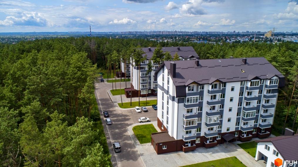 Житловий комплекс Ідея: багатоповерхові будинки з біло-сірими фасадами та коричневими дахами, оточені сосновим лісом.