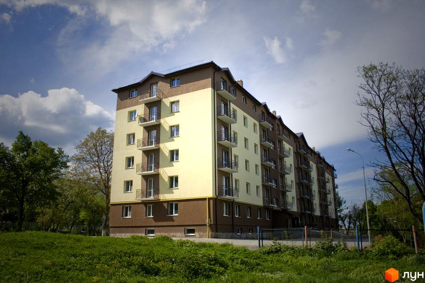 Житловий комплекс Підгір'я – багатоповерховий будинок з балконами та вікнами на тлі неба та зелені. Навколо новобудови розташовані дерева та трава.