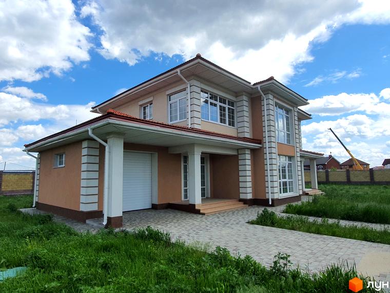 Двоповерховий будинок з гаражем у Котеджному містечку Осокорки. Подвір'я вимощене бруківкою, навколо зелений газон.