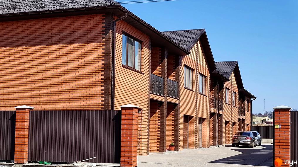 Зовнішній вигляд таунхаусів з червоної цегли з темним дахом. На передньому плані коричнева огорожа та доглянута територія Житлового комплексу „Екологічний“.