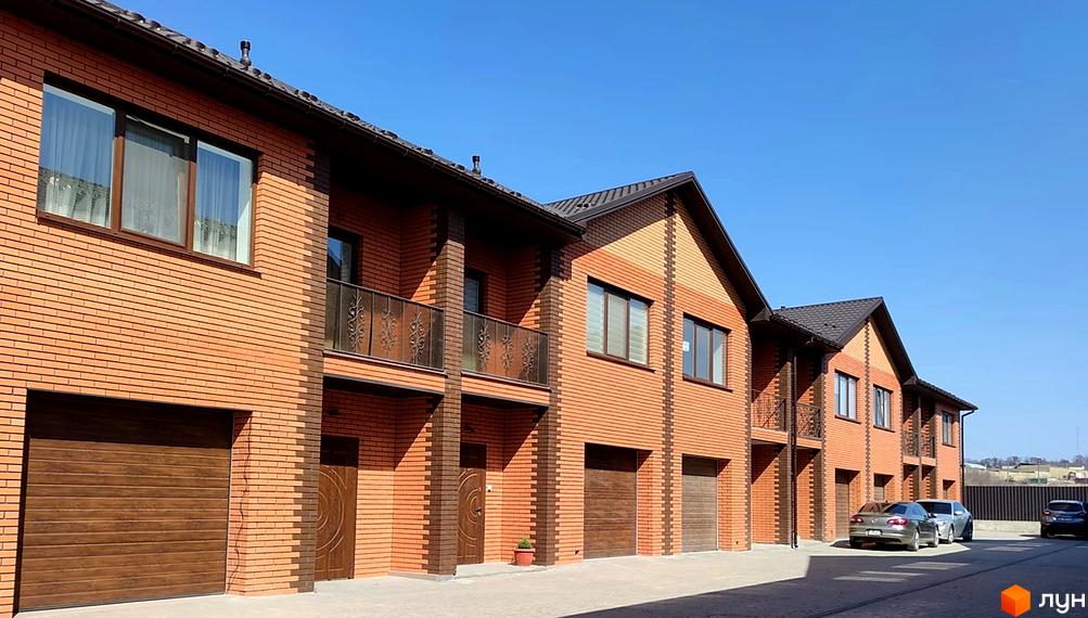 Зображення фасаду таунхаусів Екологічний (Гоголя) з червоної цегли. Перед будинком припарковані автомобілі.