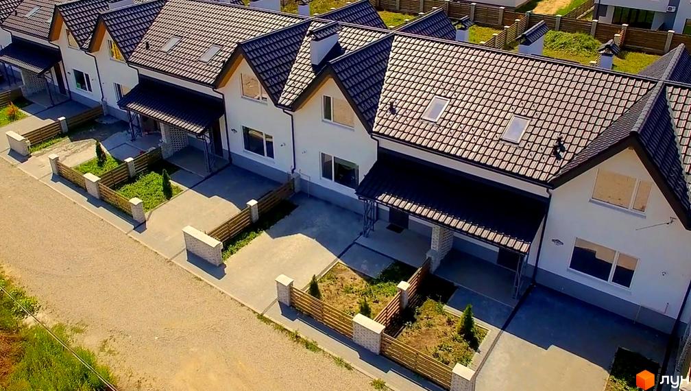 Зображення таунхаусів «Екологічний» з чорними дахами та білими стінами. Навколо будинків зелені насадження та акуратні паркани.