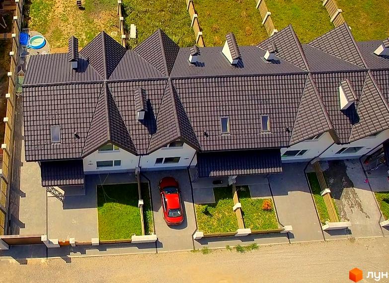 Зображення таунхаусів „Екологічний“ (Рибацька) з темним дахом та білими стінами. На подвір'ї газон та червоний автомобіль.