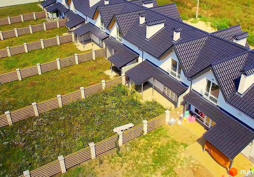 Вигляд на таунхауси з темними дахами та білими стінами. Навколо кожного будинку є зелена ділянка з дерев'яним парканом.
