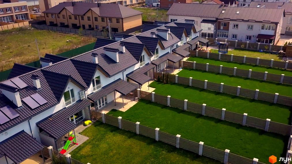 Вид на таунхауси з темними дахами та білими стінами. Навколо будинків зелені газони, огороджені дерев'яними парканами.