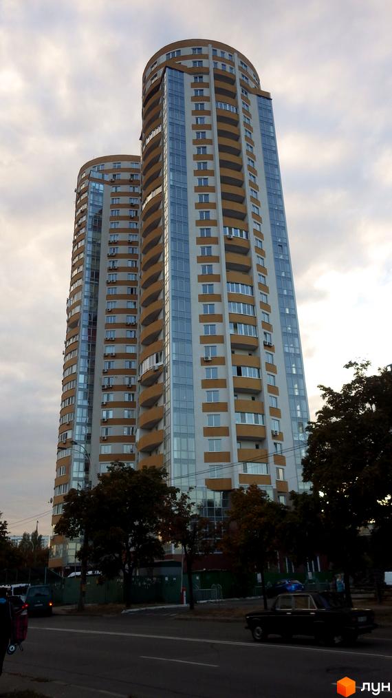 Житловий комплекс Барвінок з двома висотними будинками. Прибудинкова територія озеленена деревами та має асфальтовану дорогу.