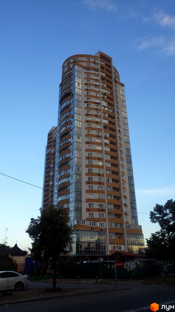 Житловий комплекс Барвінок з сучасним фасадом та великими вікнами. Прибудинкова територія з зеленими насадженнями та паркувальними місцями.