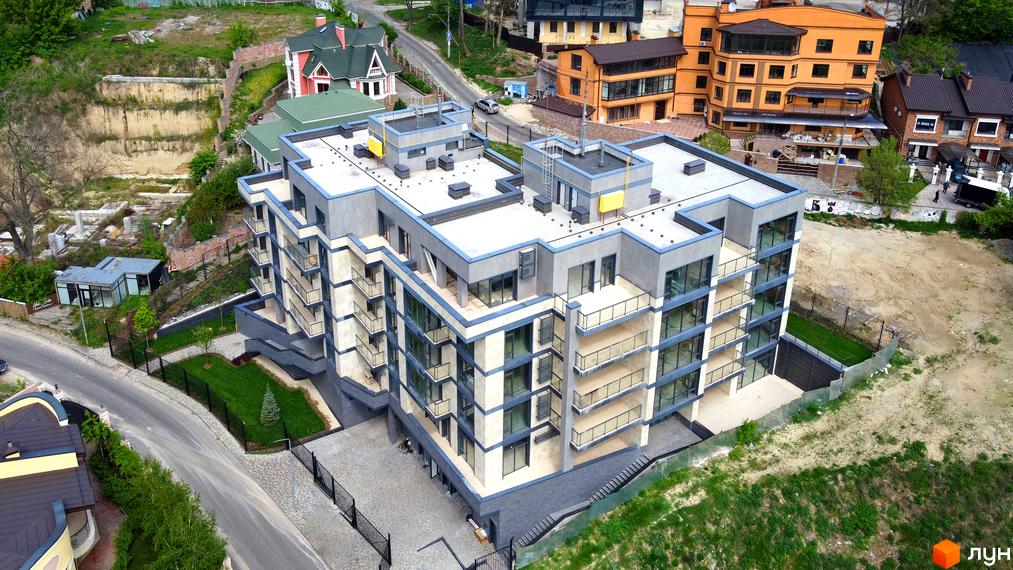 Зображення чотириповерхового Клубного будинку „InCo Home на Подолі“ з сірим фасадом та скляними балконами. Навколо будинку зелена територія з газоном та доріжками.