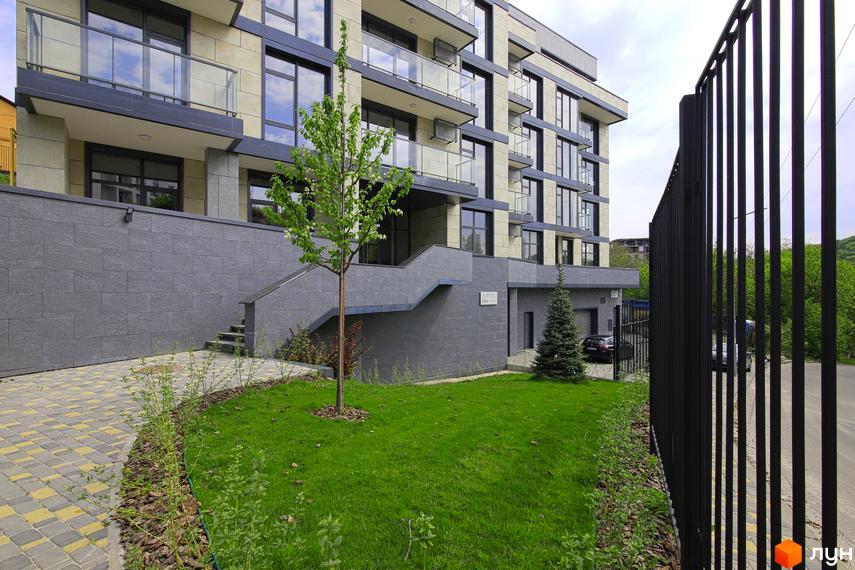 Зображення фасаду Клубного будинку „InCo Home на Подолі“ з прибудинковою територією. Вигляд будинку з газоном, деревами та пішохідною доріжкою.