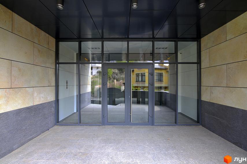 Фасад будинку Клубний будинок „InCo Home на Подолі“ з великими вікнами та скляними дверима. Оздоблення стін виконано з каменю світлих та темних відтінків.