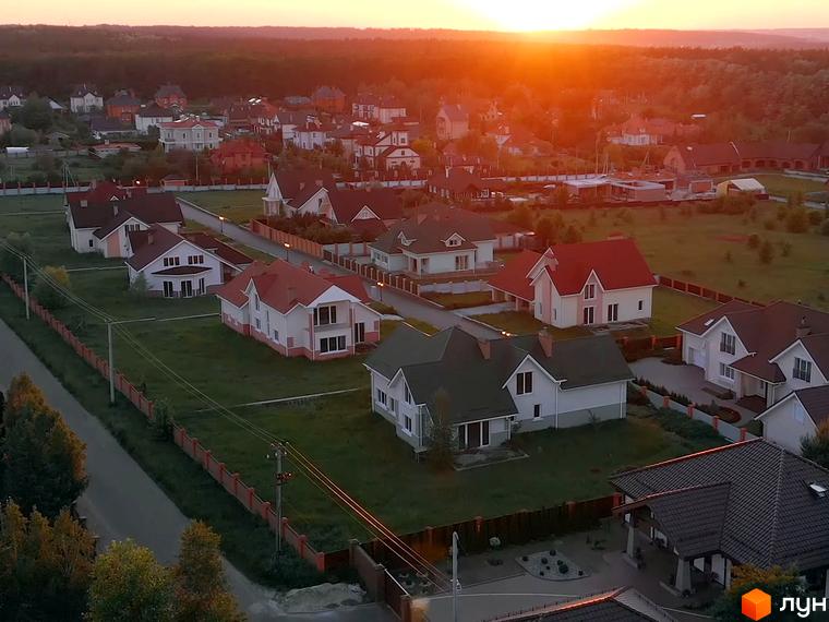 Котеджне містечко На узліссі: сучасні будинки з червоними дахами та доглянутою прибудинковою територією на тлі заходу сонця. Продаж новобудов у мальовничому місці.