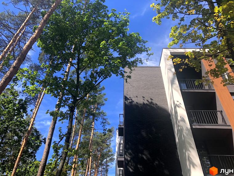 Житловий комплекс Forest Park з фасадом з темної цегли та білими елементами. Навколо новобудови зелені дерева та синє небо.